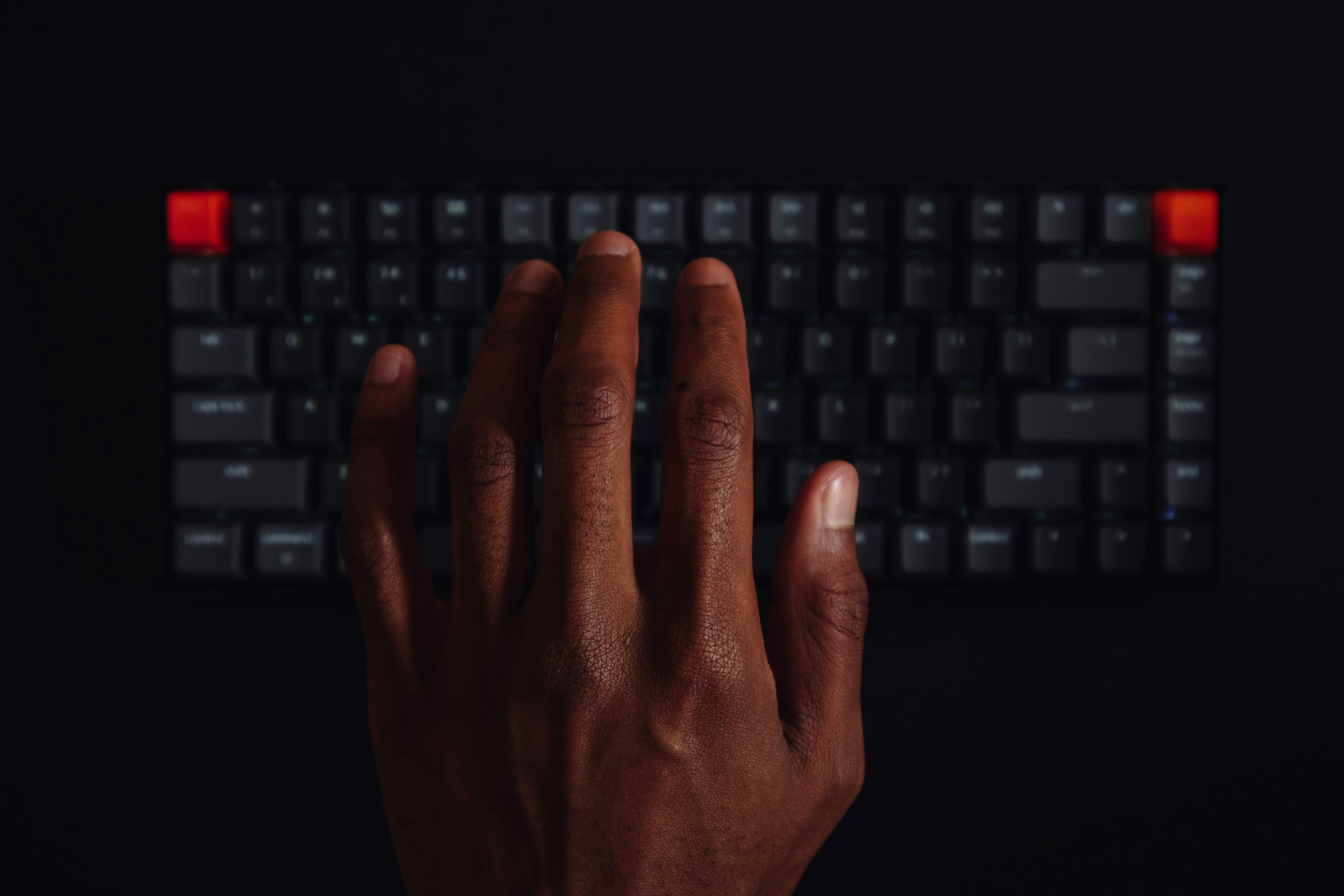 A hand resting on a dark keyboard in low light.