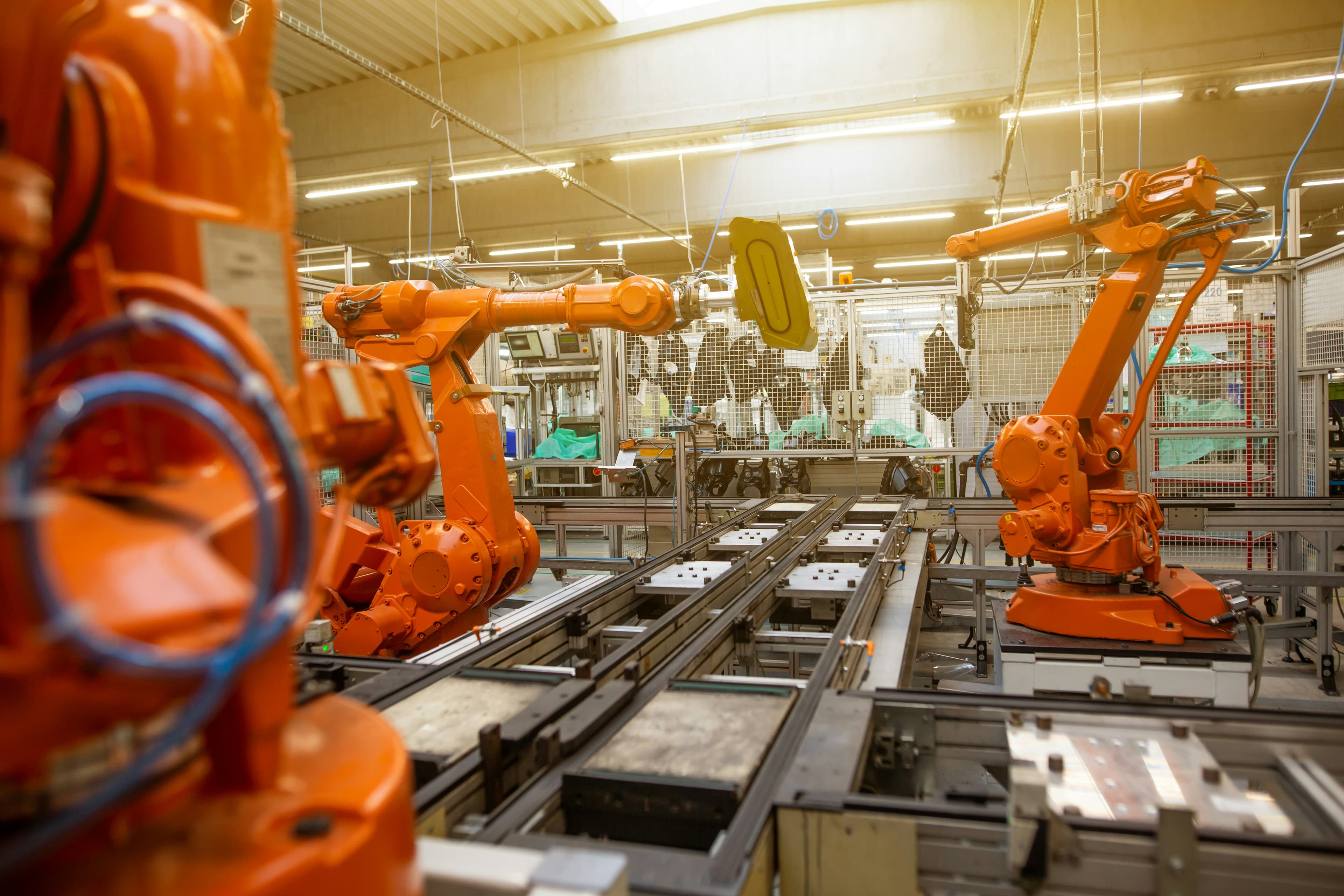 Orange industrial robot arms working along an automated assembly line in a factory.